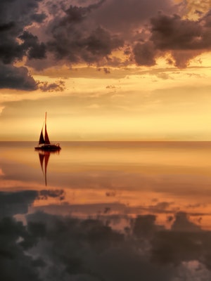A sail boat to the side in the ocean at dusk.