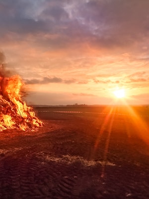 Camera shot straight at the sun with a house on fire in the background